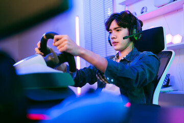 Asian male pro gamer playing an online car drive simulation game with steering wheel controller. Gamer focus an sports game with concentrate emotion. The player rejoices in victory in the competition.