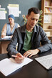 © Seventyfour - Vertical shot of adult multiracial male student focused on writing task sitting at desk in study group during class while taking courses in language school