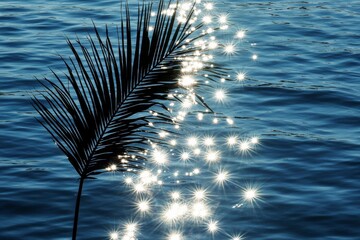 Poster - A palm leaf silhouette is seen against a background of shimmering water, where sunlight creates a sparkling effect, conveying a serene tropical ambiance.