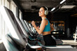 © Home-stock - Happy European woman in sportswear and wireless headphones doing hard cardio workout on treadmill, lady running in empty gym