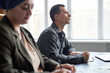 © Seventyfour - Side view of thoughtful adult multiracial man looking attentively at blackboard listening to teachers advice, while writing in notebook sitting at desk in language course group