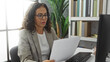 © Krakenimages.com - Woman reading document in office setting with bookshelf in background, wearing glasses and blazer, suggesting professional environment and focused demeanor.