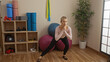© Krakenimages.com - Woman exercising in a gym with yoga mats and fitness equipment, blonde adult performing workout in a spacious interior with wooden floor and indoor plants.