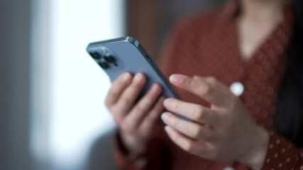 Close up of female hands using mobile phone in modern living room. Young asian woman engaged in digital communication, browsing social media or chatting online. Concept of technology usage, connection