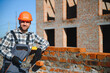 © Serhii - construction mason worker bricklayer installing red brick with trowel putty knife outdoors