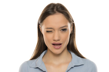 Wall Mural - Portrait of a beautiful young winking woman with makeup on a white studio background