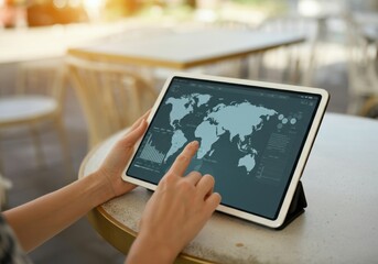 Poster - Businesswoman using digital tablet displaying interactive world map with financial charts, analyzing global market trends in a cafe