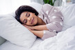 © deagreez - Young woman peacefully sleeping in comfortable polka-dot pajamas, embracing rest in cozy bright bedroom