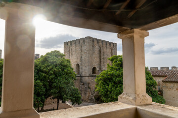 Historic stone tower of Elvas castle framed by lush trees with sunlight and columns