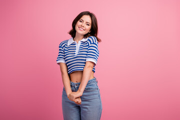 Wall Mural - Charming young woman in stylish striped polo poses with a happy smile against a pink background, displaying her casual summer fashion