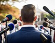 © Matilde - back view of a politician speaking at a press conference surrounded by microphones and journalists outdoors conveying leadership and media interaction