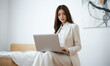 © RooftopStudioBangkok - business woman in light suit working on laptop in modern setting, exuding professionalism and focus. minimalist background enhances her concentration