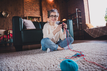 Wall Mural - Elderly woman enjoying knitting at home, smiling in daylight. Leisure time for mature female in cozy apartment interior