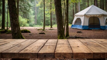 Wall Mural - A empty wooden table in the foreground with a tent and trees in the blurred background, suggesting an outdoor camping scene in a forest