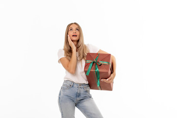 A woman thoughtfully poses with a beautifully wrapped gift in a bright, minimalistic setting while wearing casual attire