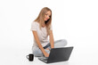 © Svetlana - A woman with long hair sits on the floor using a laptop while enjoying coffee in a bright, minimalistic workspace during the day