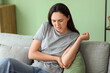 © Pixel-Shot - Young woman suffering from pain in elbow on sofa at home