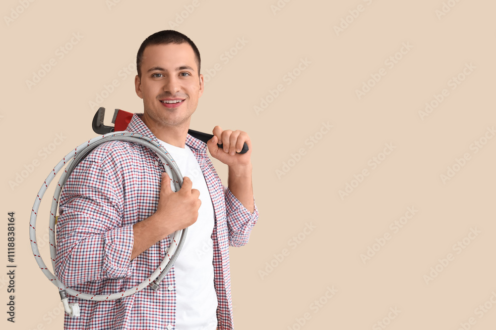 Male plumber with wrench and hose on beige background