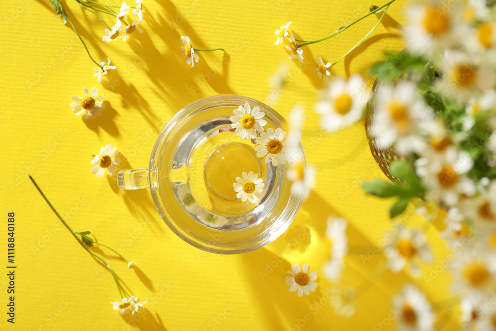Cup with water and chamomile flowers on yellow background. Top view