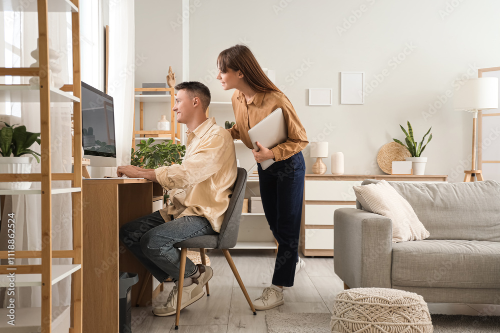 Young woman with laptop and her boyfriend using computer at home