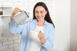 © Pixel-Shot - Beautiful young happy woman pouring hot water from kettle into cup in kitchen