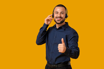 Wall Mural - Male technical support agent in headset showing thumb-up on yellow background