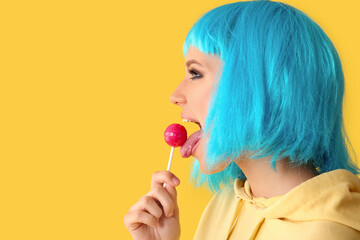 Wall Mural - Beautiful young woman in blue wig with sweet lollipop on yellow background