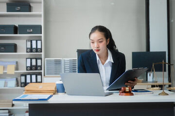 Wall Mural - A young Asian woman in a suit works at her desk, reviewing legal documents. lawyer advice on contracts, finance, agreements, demonstrating professionalism and authority in business setting.