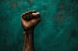 © Dhoku  Studio - Dark skinned person raising clenched fist in front of teal background