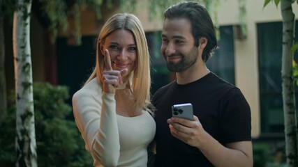 The couple watch their smartphone, using a mobile app to win a prize. Delighted by the green screen, they celebrate. The girl snaps her fingers and gestures to the camera, encouraging further use.