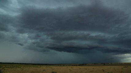 Wall Mural - dark storm clouds gather over a dry grassy field, rain falling in the distance. perfect for projects
