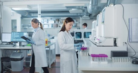 Aufkleber - Team of Young Biochemists Collaborating in a Laboratory. Asian Female Researcher Loading Test Tubes with Blood Samples Into a Centrifuge while Her Coworker Reviews Experimental Data on a Computer