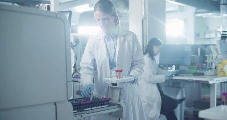 Poster - Female Hospital Doctor in White Lab Coat Operates Advanced Testing Machine, Carefully Loading a Tray of Blood Samples. Modern Laboratory Research and Analysis Facility with Team of Scientists at Work