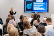 © Anton Gvozdikov - Blurred image of people listening to a business presentation in a conference setting. The speaker is presenting informative slides to an attentive audience eager to learn and engage.