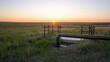 © CreativeBro - Fenced water station in a serene field with sunset over the horizon and clear sky reflecting tranquility and nature's beauty.