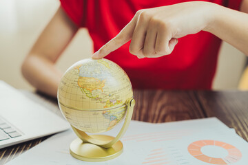 Poster - Exploring globe while analyzing data on desk, showcasing global awareness and research. hand points to specific location, emphasizing curiosity and discovery
