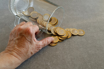 Wall Mural - A hand pours gold coins from a glass jar onto a grey surface.