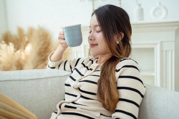 Wall Mural - Young Asian woman enjoying reading book in living room at home