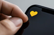 © Marut - close up of hand placing yellow heart icon on smartphone screen, symbolizing love and connection. image captures moment of affection and digital interaction