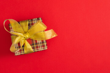 Wall Mural - Top view of bright red checkered gift box decorated with luxurious golden ribbon on red background. Greeting holiday background. Festive red background with gift. 