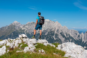 hiker man overlooking pristine rugged mountain peaks of western julian alps, italy, europe. wild hik