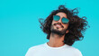 © Vivid_Vision - a happy young man with long curly hair and sunglasses on a blue background. Concept with copy space.