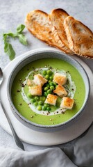 Wall Mural - Delicious pea cream soup with bread cubes and toasted baguette slices on a light gray background