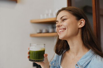 Wall Mural - Smiling young woman enjoying a green smoothie in a stylish kitchen, showcasing healthy eating and a vibrant lifestyle