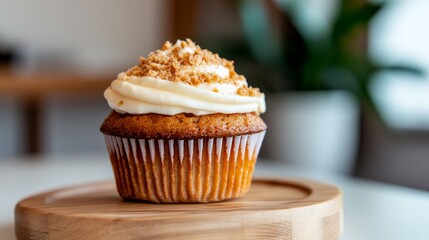 Poster - A close-up view showcases a single carrot cake muffin adorned with cream cheese frosting and crushed nuts, placed on a wooden plate in a blurred kitchen