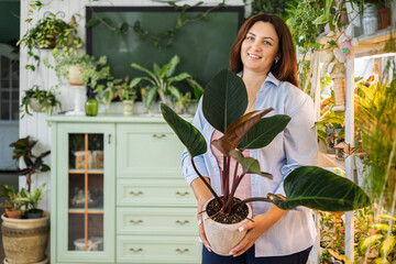 Wall Mural - Smiling woman florist gardener with philodendron at indoor home garden closeup