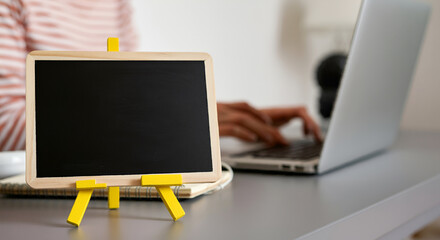 view of work from home or remote work
workspace environment dispicting a female freelancer working on laptop with blank chalkboard or frame, headphone and notebook