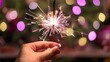 © Ari - A hand holding a firework, positioned slightly off-center with a glowing star pattern. The background has a soft bokeh effect in soft pinks, purples, and greens, evoking a festive holiday atmosphere.