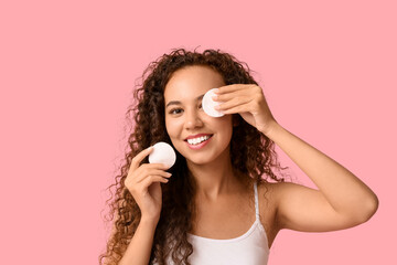 Wall Mural - Beautiful young African-American woman with healthy moisturized skin holding cotton pads on pink background