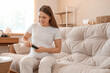 © Pixel-Shot - Young pregnant woman with gestational diabetes using glucometer on sofa at home